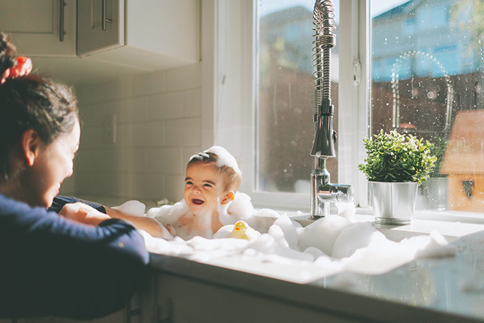 Baby getting a bath in the kitchen sink.