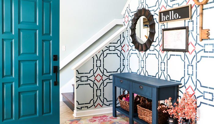 Teal blue front door opening to entryway with bold geometric wallpaper.