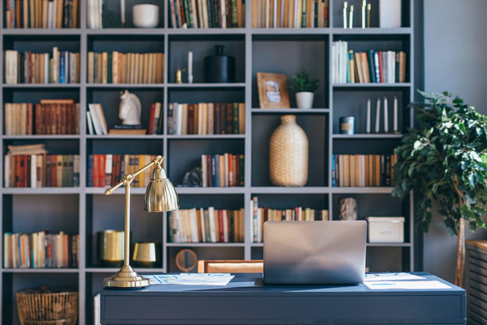 Home office with bookcase desk lamp and laptop.