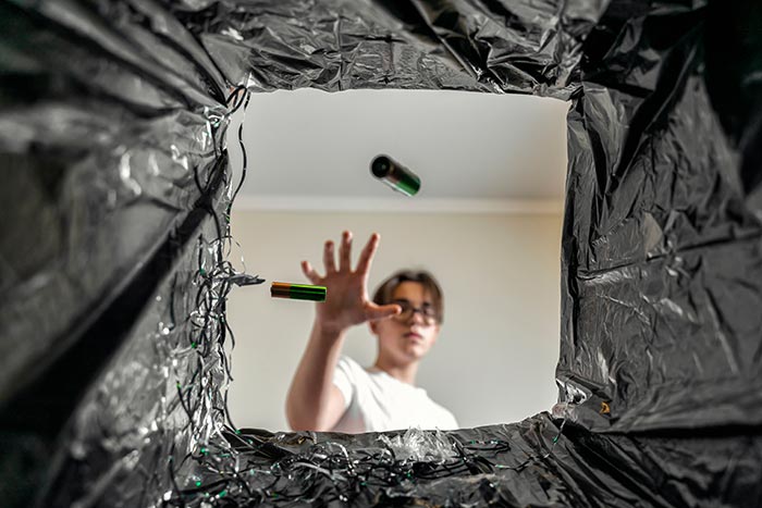 Man throwing batteries into trash can.