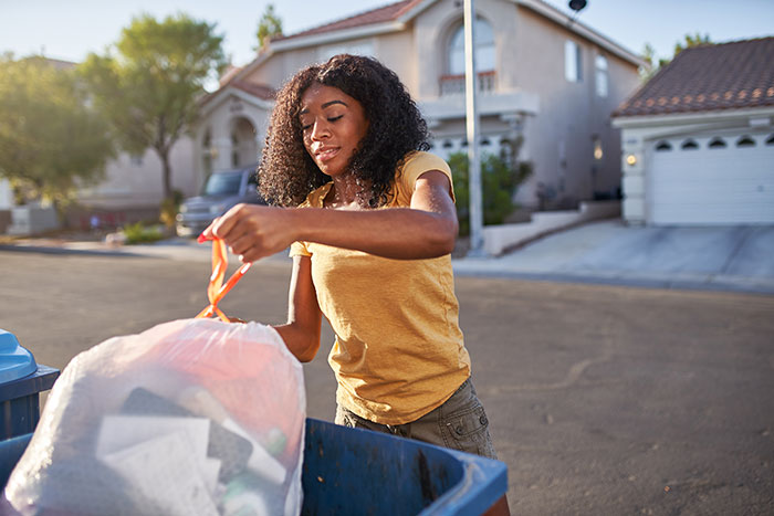 Woman placing trash bag in trash toter on residential street.