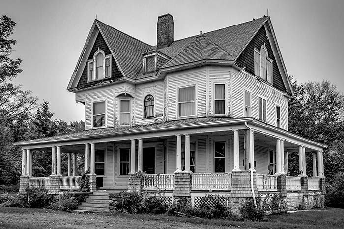 Black and white photo of Victorian home with peeling paint.