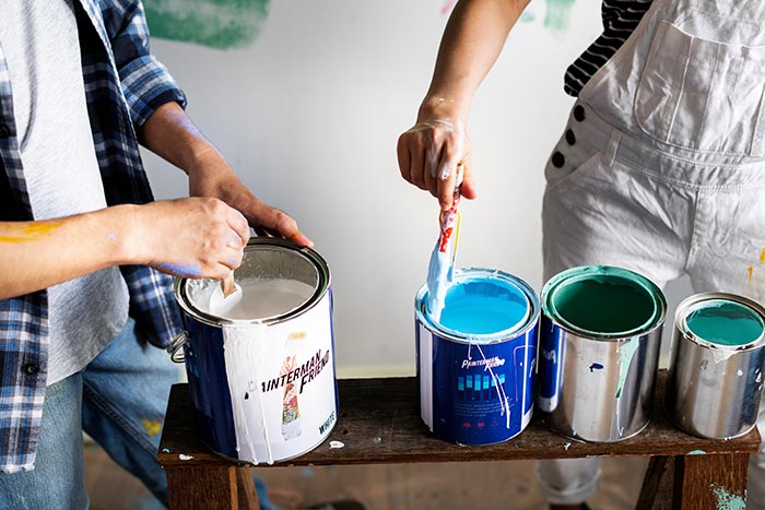 Two people dipping paint brushes into paint cans.