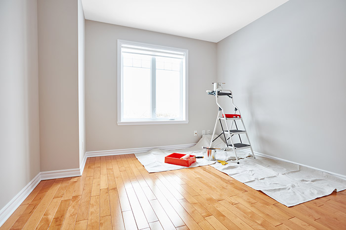 Empty room set up with paint supplies, drop cloth and step ladder.