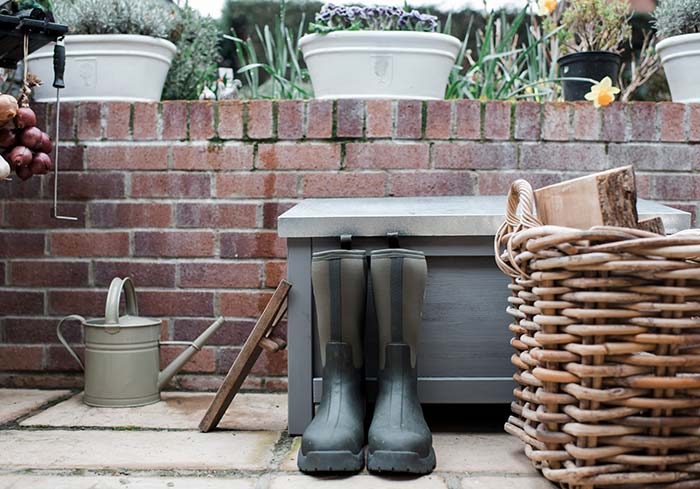Garden rain boots next to basket and flower bed.