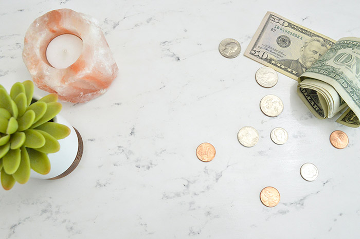Cash money and coins laying on marble kitchen counter next to Himalayan salt lamp and green plant.