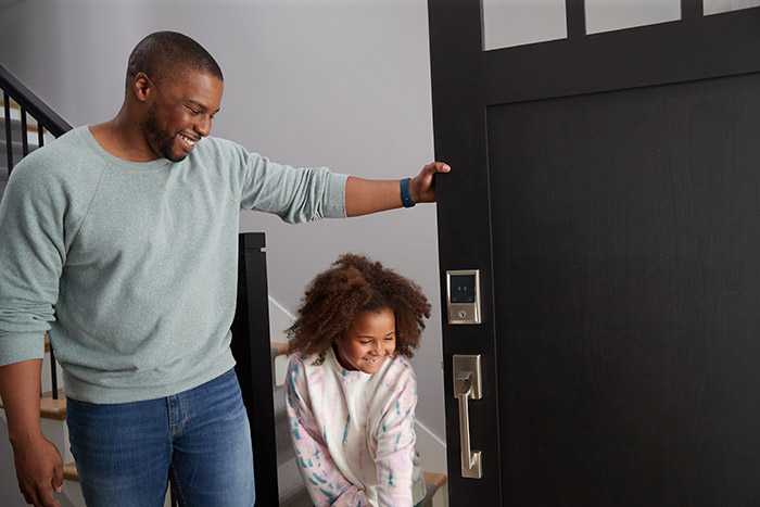 Dad wearing Apple watch, holding front door open for daughter with HomeKit door lock.