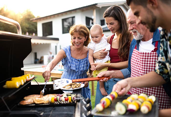  Family standing over grill during backyard summer party.