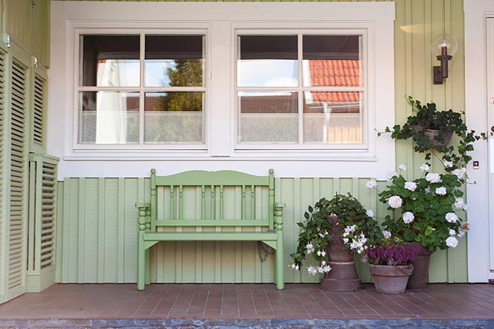 Cozy cottage front porch with green bench and fresh white flowers.