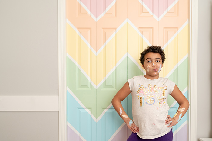 Young girl standing next to Chevron painted bifold closet doors.