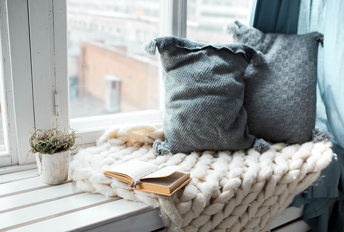 Cozy reading bench by window with chunky knit throw and pillows.