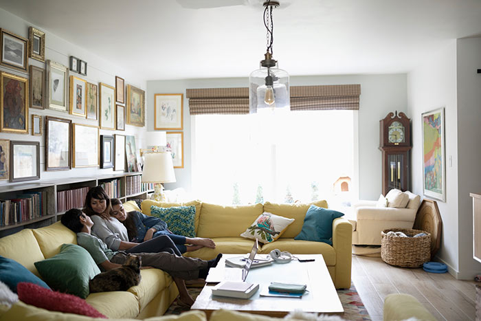 Mother relaxing at home on a yellow couch with two older children in eclectic living room.