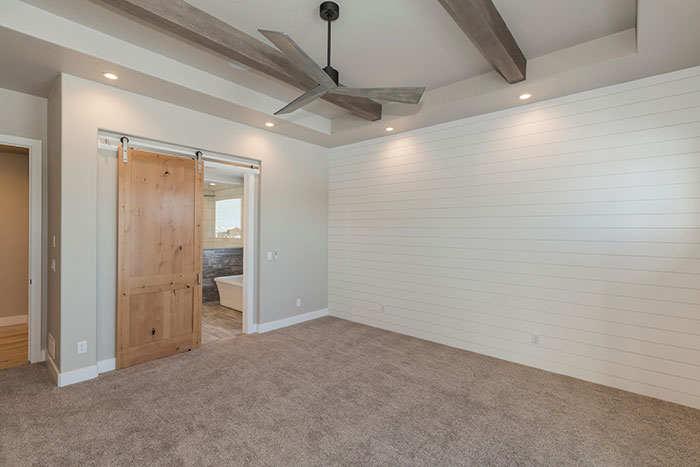 Empty modern farmhouse bedroom with shiplap wall and sliding barn door.