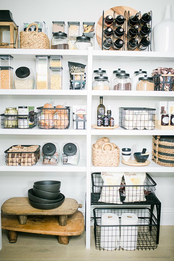 Monochromatic organized kitchen pantry with black baskets and jars.