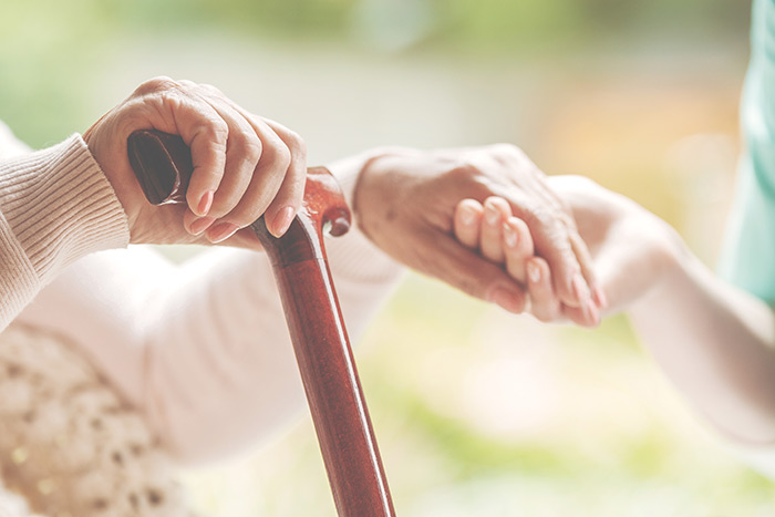Person with cane holding hand of caregiver.