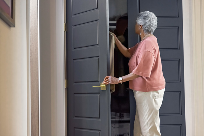 Woman reaching into closet with grey closet door and satin brass door handle from Schlage.