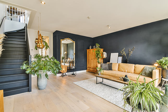 Bold living room with matte black walls and natural materials, hardwood floors, wood cabinet, and green plants.