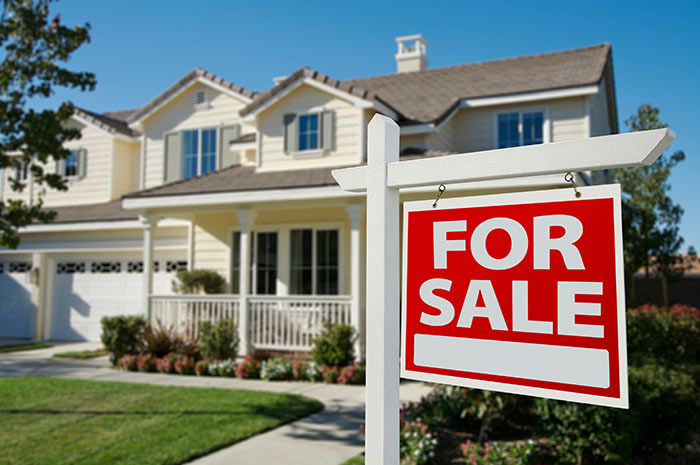 Light yellow suburban home with red for sale sign in front.