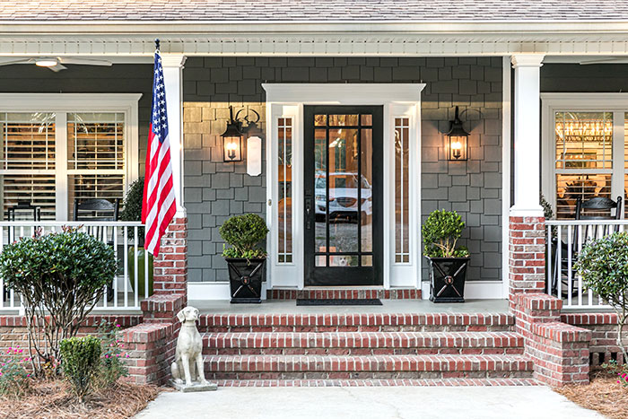 Grey home with black front door, sidelights, and brick porch steps.