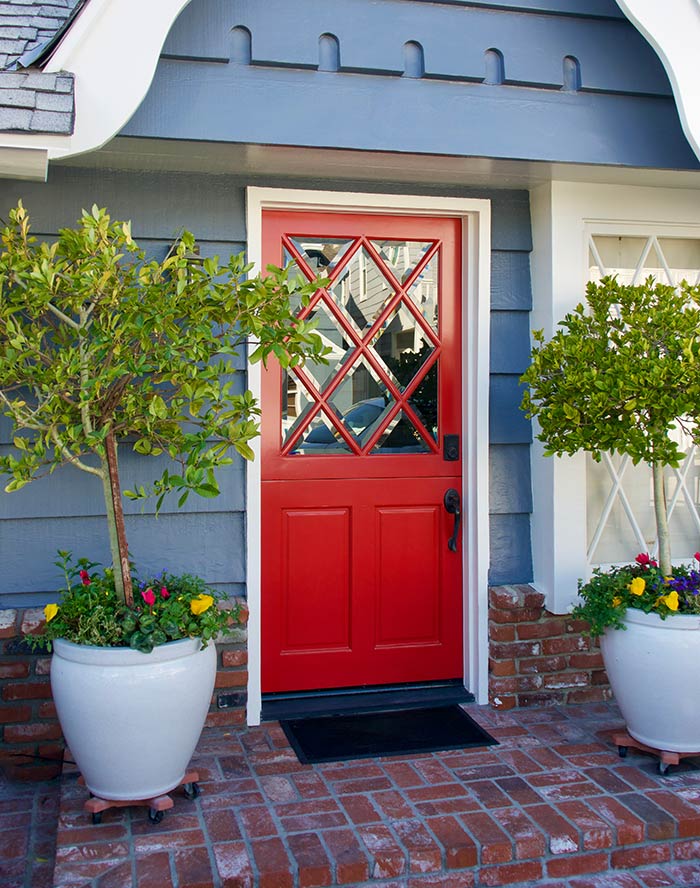 Red dutch door with glass panes on blue home with large planters.