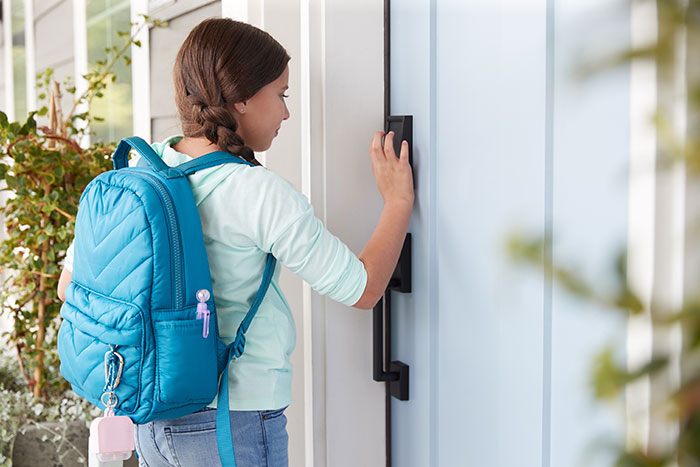 Young girl arriving home from school using smart lock on front door.