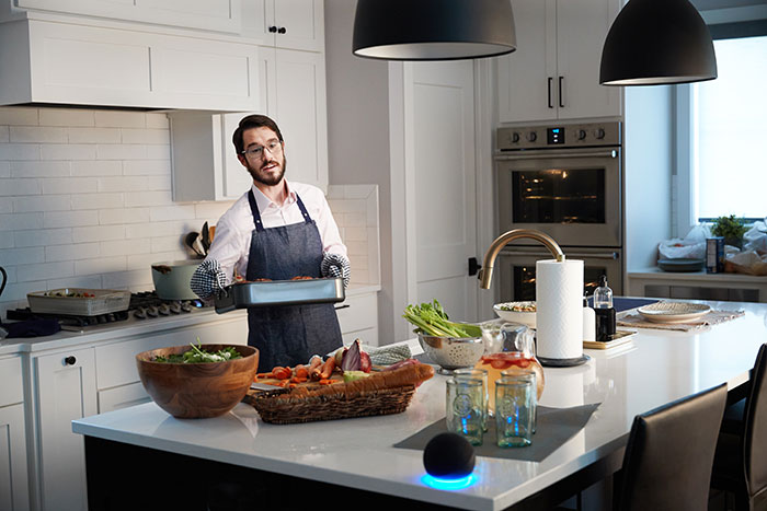 Man cooking in kitchen speaking to Amazon Alexa speaker.