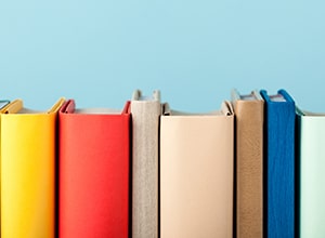 Row of colorful books against light blue wall.