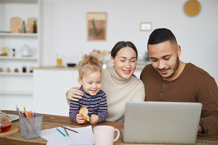 Family sitting together at table looking at computer.