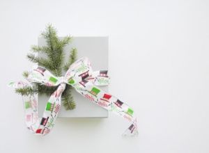 White gift box wrapped with holiday ribbon and Christmas greenery.
