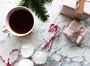 Mug of coffee next to candy canes and holiday packages on marble countertop