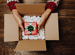 Shipping box with packing peanuts and red and green holiday gift box.