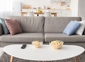 Two bowls of popcorn on white coffee table next to grey couch.