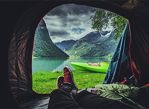 Person laying in tent enjoying view of mountains and water.
