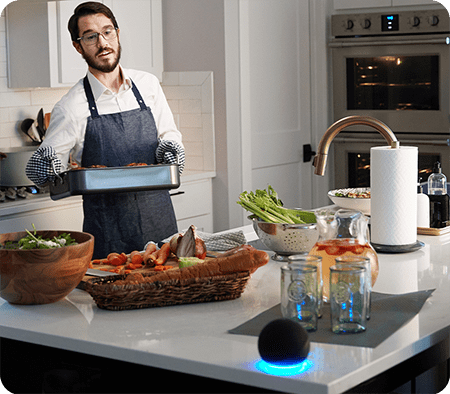 Man cooking in kitchen and speaking to voice assistant smart speaker.