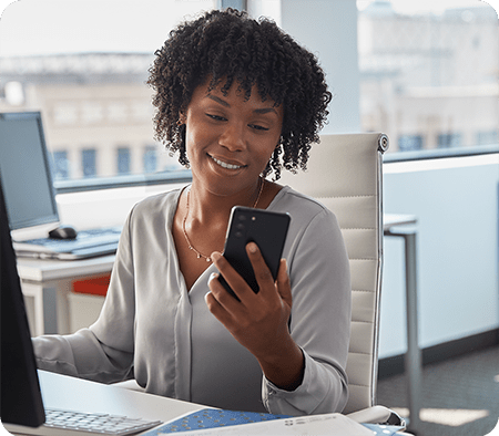 Woman sitting in office checking Schlage Home app on her smartphone.