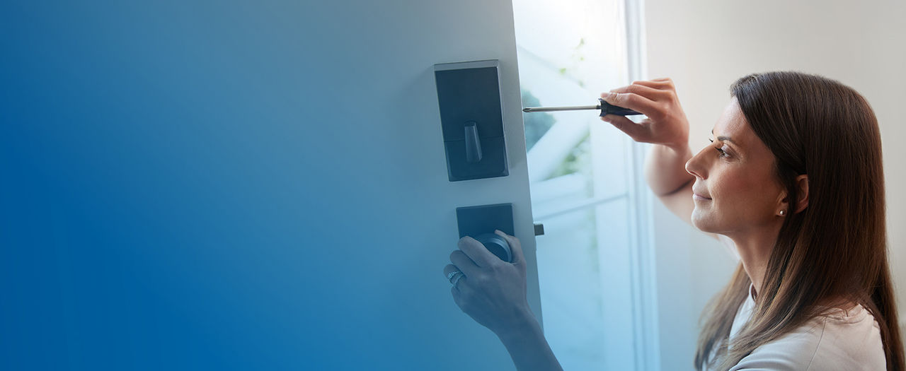 Woman installing smart lock on front door.